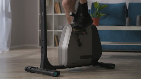person-is-training-alone-in-home-using-stationary-bike-for-keeping-fit-closeup-of-legs-on-pedals-fitness-and-wellness-concept
